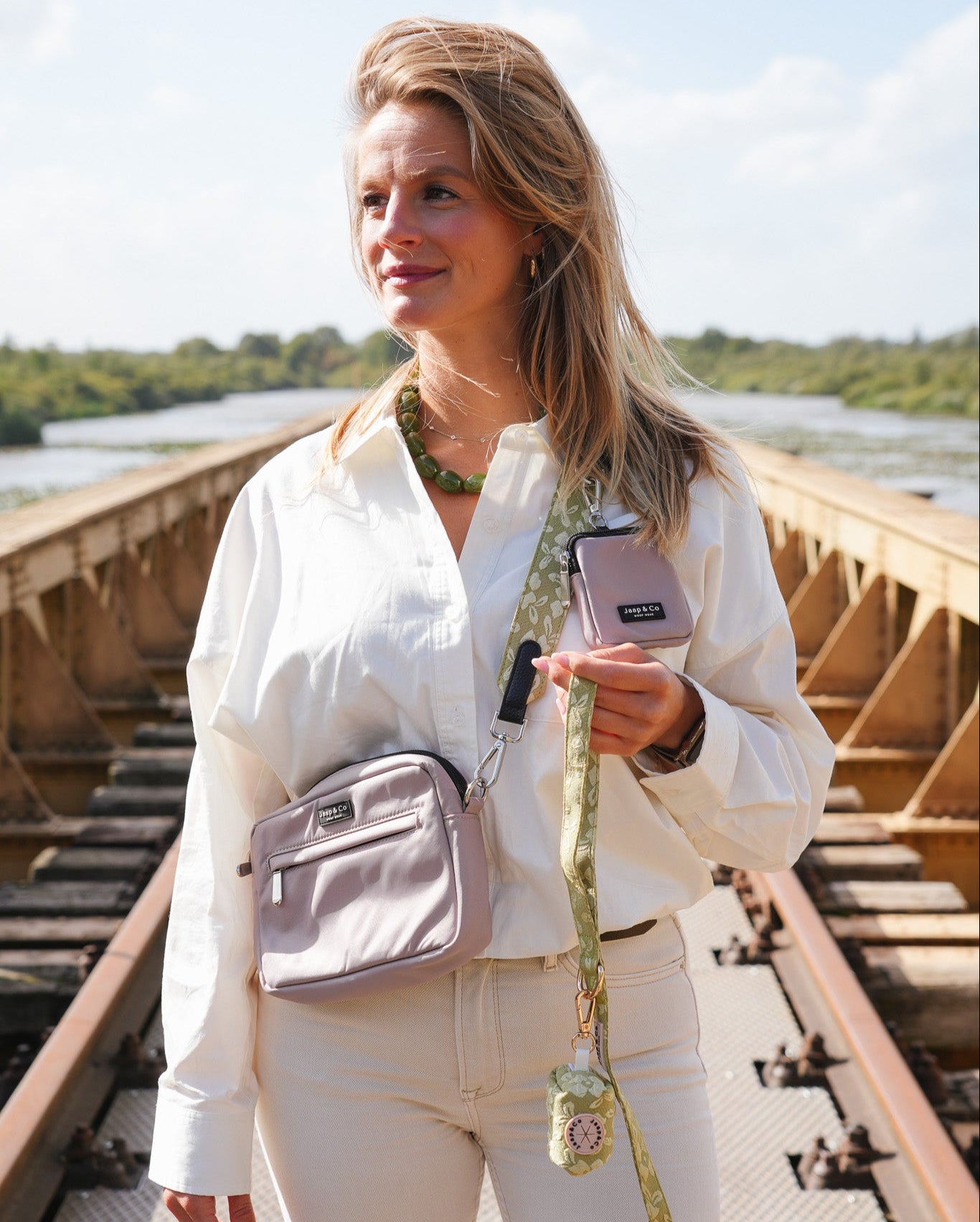 Model met de Latte Machiato dogmom bag en treatpouch gecombineerd met de Botanical Glow collectie, een lichtgroene kleur met lichtere geborduurde bloemenprint: strap, riem en poepzakjeshouder