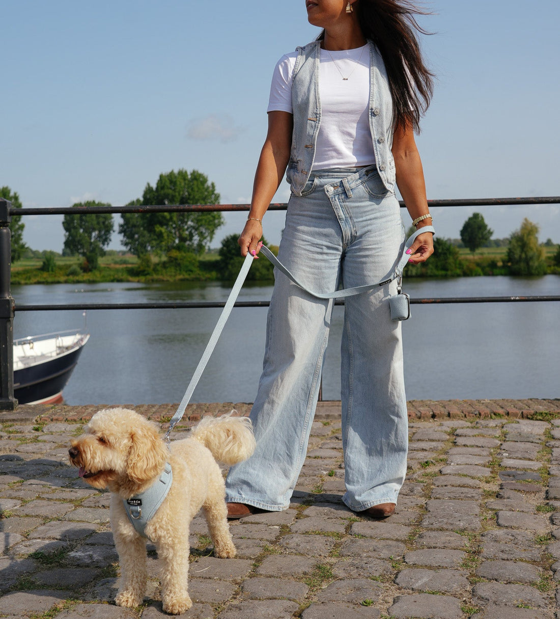 Vrouw met haar hond match haar denim outfit met de Jaap & Co Denim Days collectie; een mooie lichtblauwe denim kleur hondentuigje, riem en poepzakjeshouder