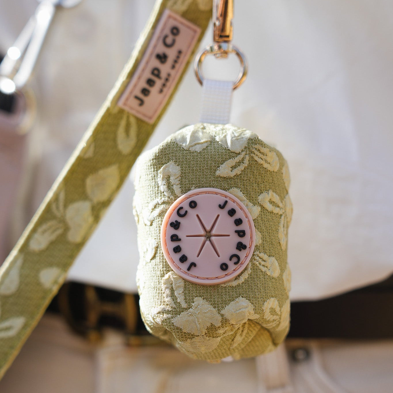 Foto waar het poepzakjeshouder aan de riem bevestigd zit. Een mooie lichtgroene collectie met lichtere bloemen op geborduurd van de Botanical Glow collectie van Jaap & Co