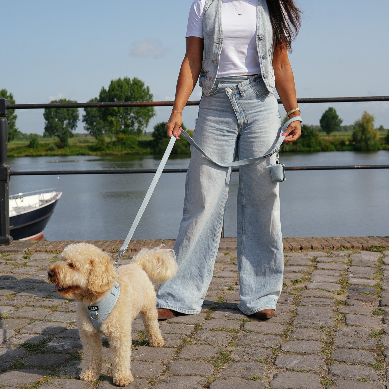 Baasje draagt denim outfit en matcht met hond. Hond draagt lichtblauwe denim kleurige tuig, riem en poepzakjeshouder van de Jaap & Co Denim Days collectie