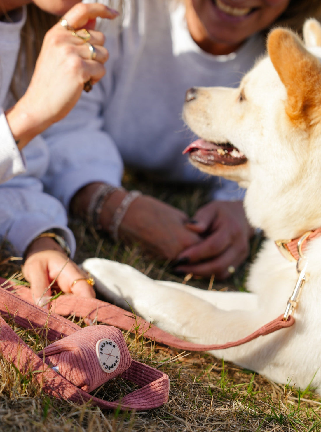 Vrouw ligt met haar hond aan de koraalkleurige corduroy riem uit de Jaap &amp; Co Golden Trails collectie, inclusief poepzakjeshouder en goudkleurige metalen details, in warm nazomerlicht.