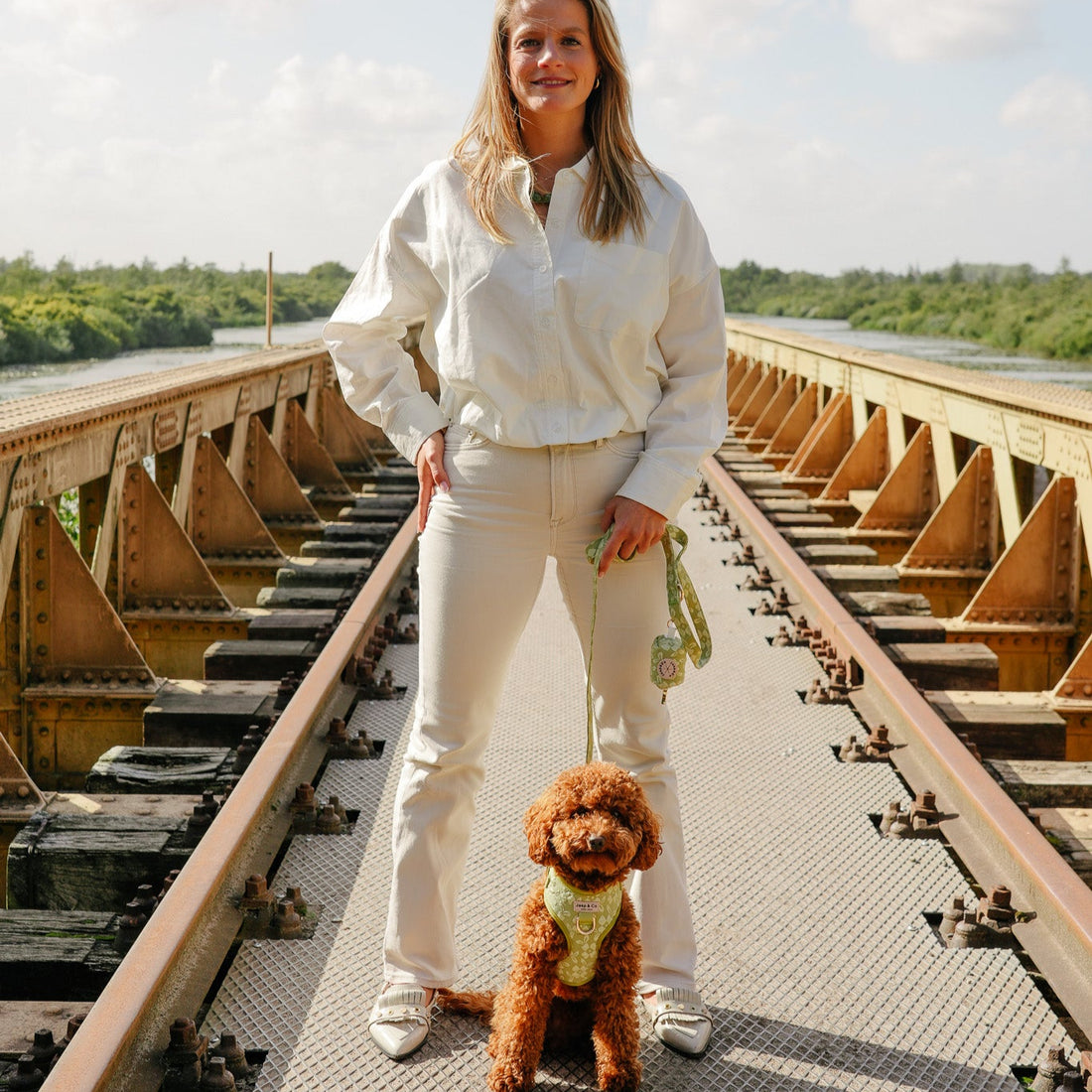 Foto van baasje samen met labradoodle hond. Hond draagt het Botanical Glow tuigje, riem en poepzakjeshouder, een mooie lichtgroen design met geborduurde bloemen van Jaap &amp; Co