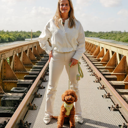 Foto van baasje samen met labradoodle hond. Hond draagt het Botanical Glow tuigje, riem en poepzakjeshouder, een mooie lichtgroen design met geborduurde bloemen van Jaap &amp; Co